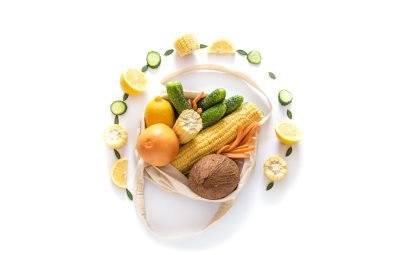 Grocery shopping with eco bag over white background. Zero waste and plastic free concept. Coconut. bananas, lemons, orange, carrot, cucumber, greens. Flat lay. Copy space
